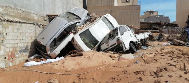 Three cars piled against a wall amidst flood devastation